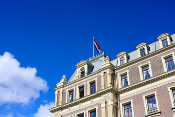 Fototapeta na wymiar Dutch national flag hanging on the exterior facade of Amstel hotel with vibrant blue sky and clouds in the background. Amsterdam, The Netherlands. 