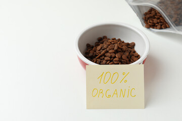 Pack and feeding bowl of dry cat food with note 100% Organic on white table. Space for text