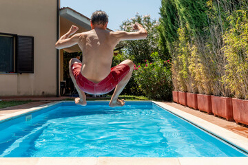White man, shot from behind, throws himself into the pool on a hot summer day