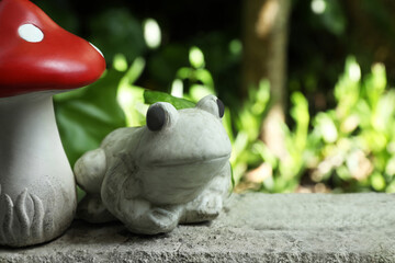 Frog figure and decorative fly agaric on stone parapet outdoors. Space for text
