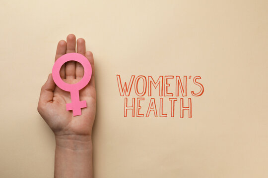 Girl holding female gender sign near text Women's Health on beige background, top view