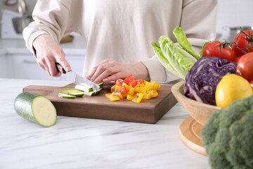 Woman cutting fresh vegetables at table in kitchen, closeup