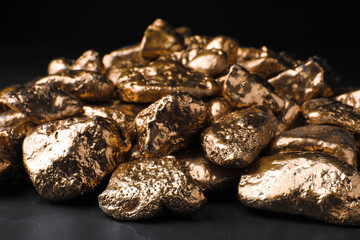Pile of gold nuggets on black table against dark background, closeup