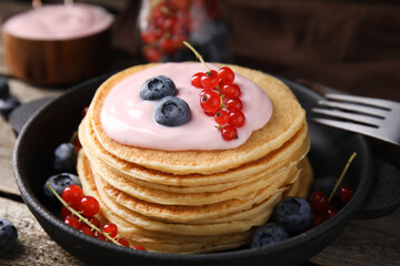 Tasty pancakes with natural yogurt, blueberries and red currants on wooden table, closeup