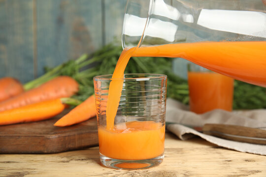 Pouring freshly made carrot juice into glass on wooden table
