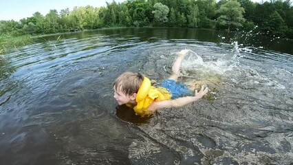 Baby boy in inflatable safety life vest floating at lake with splashing water drops slow motion