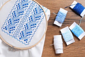Shirt with blue embroidery design in hoop and threads on wooden table, flat lay. National Ukrainian clothes © New Africa