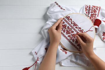 Woman embroidering shirt with red thread at white wooden table, top view and space for text....