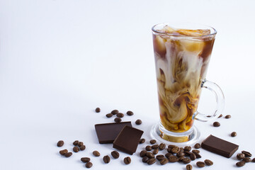 Cold brew coffee with milk in the glass and coffee beans, pieces of chocolate on the white background. Closeup. Copy space.