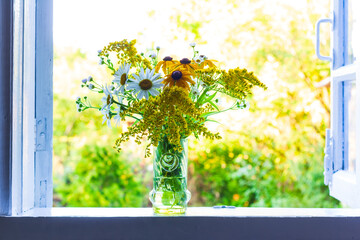 a beautiful bouquet of wildflowers on the windowsill at an open window in a village house on a summer evening - 520641798