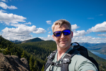 Naklejka premium An adventurous athletic male hiker taking a selfie with a large lake and mountains in the background in the Pacific Northwest.