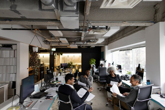 Business people with paperwork meeting in circle in open plan office
