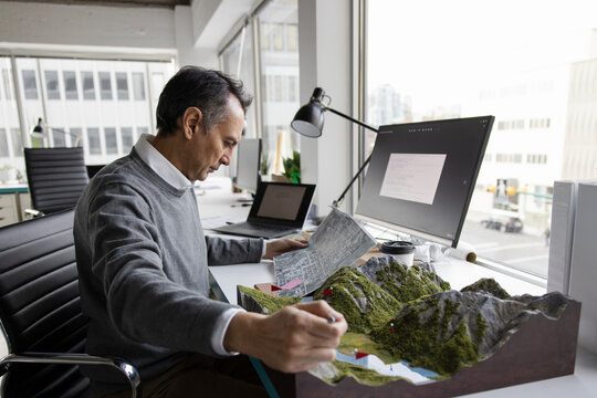 Male architect with landscape model working at office desk