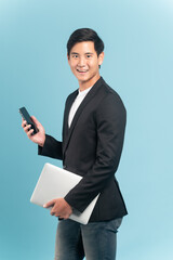 Young asian businessman in smart casual style using smartphone and holding a laptop isolated on blue background