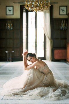 Bride in a dress sits on the floor near the window of an old villa