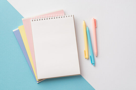 Back to school concept. Top view photo of colorful school supplies open copybook and colorful pens on bicolor blue and white background with copyspace