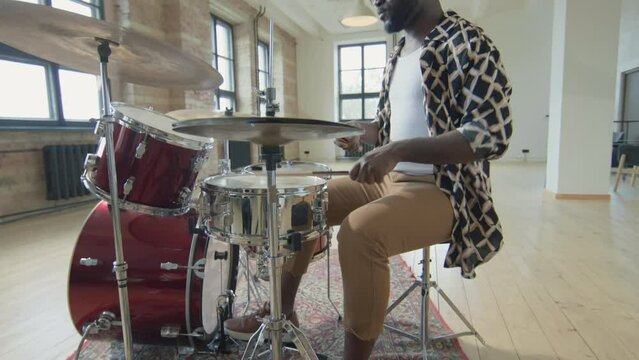 Tilt up shot of professional African American drummer playing drums with enjoyment in spacious loft studio
