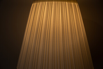 The fabric lampshade of the sconce is illuminated from the inside by the dim light of a light bulb