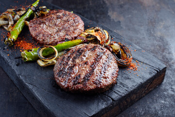 Barbecue Wagyu Rindfleisch Hamburger Patties mit gegrilltem Chili und Zwiebelringen serviert als close-up auf einem verkohlten Holz Board
