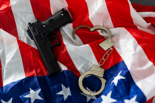 Gun, holster, and handcuffs in front of the American flag, horizontal.