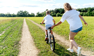 loving mother help her cute son ride a bicycle