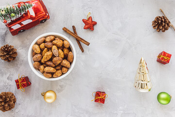 Candied or sugared almonds with honey and cinnamon in bowl on gray with Christmas decoration background. Traditional Christmas sweets for holidays. Top view, copy space