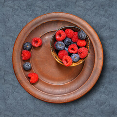 Berries, raspberries and blueberries, in a clay bowl on a black table. View from above - 520647948