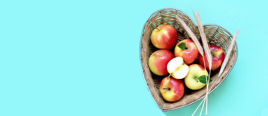 Red apples and ears of wheat in straw basket made in the shape of heart on green background. Religious holidays concept - Jewish New Year or Transfiguration of the Lord. 