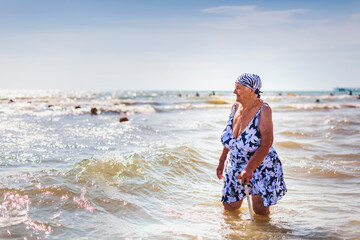 An old woman in a bathing suit with a cane went into the sea knee-deep