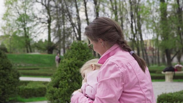 In a city park, a mother hugs and kisses her daughter.