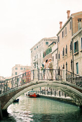 Bride and groom stand on a stone bridge over a canal against the backdrop of old houses in Venice