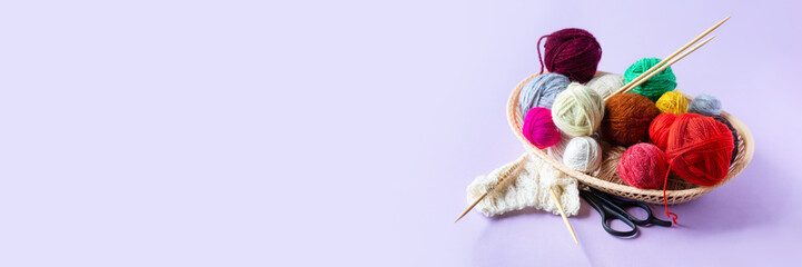 Red, yellow, white, purple, brown, green balls of thread in a beige basket with knitting needles...