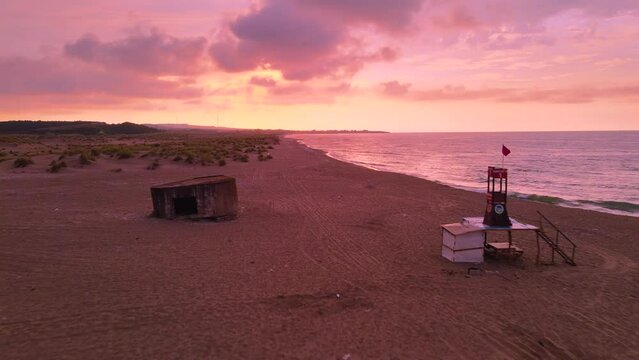 Aerial footage on a beach at sunset camera moving forward west to the sun in the horizon Black Sea coastline Karasu Sakarya Turkey lifeguard tower cloudy weather summer purple and orange colors