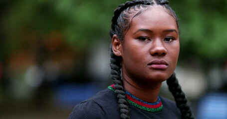 Serious young black woman looking at camera outside. Dramatic African girl staring viewer