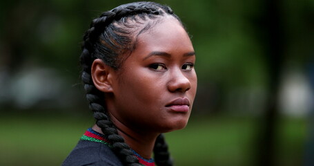 Serious young black woman looking at camera outside. Dramatic African girl staring viewer