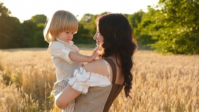A mother with a baby walks in a wheat field in the summer at sunset. New grain crop.