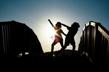 Boy and girl silhouettes dancing on a bridge