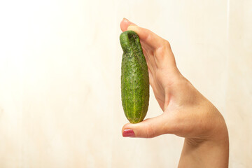 Mature woman's hand, with red nails, holding a wrinkled cucumber or pickle.