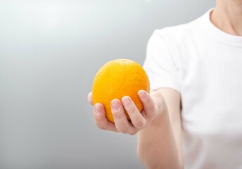 A woman's hand in a white T-shirt holds an orange.