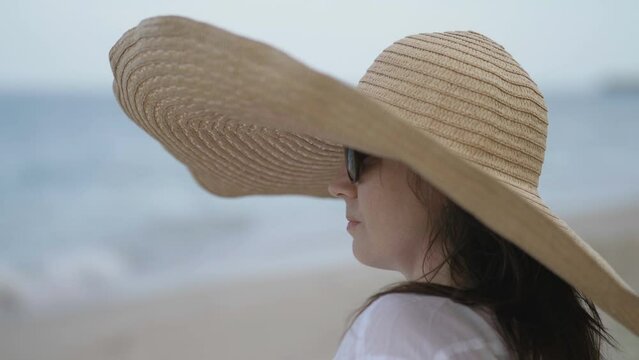 Portrait of woman with large brim hat and glasses watching the sea