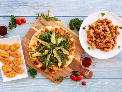 Assorted fastfood Avocado Rockets Pizza, Crispy Nuggets With BBQ Dips, Popcorn Chicken Served in dish isolated on wooden table top view fastfood