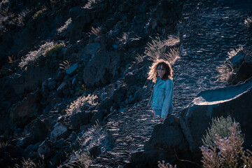 Young woman with curly hair trekking on a rock path in sunset light