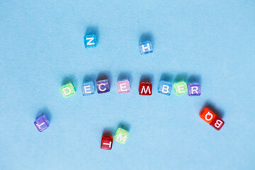 inscription december made by multicolor plastic cubes on a blue background.