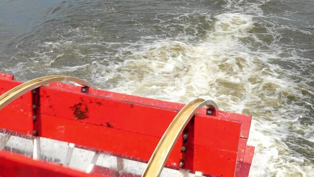 Rotating red wooden paddle wheel of a tour boat in motion on the water, in closeup handleld clip with zoom in to blurred water.