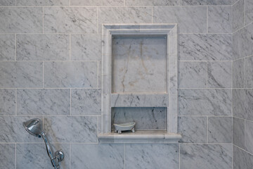 Luxury shower with gray and white marble wall featuring soap inset and chrome finishes. 