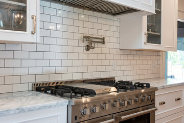Modern kitchen details of granite counter, large gas stove, tile backsplash, and pot filler faucet.