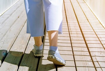 Close-up of women's feet in sports shoes walking on a wooden bridge on a sunny day. Tinting, selective focus.
