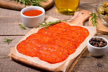 Chorizo sausage and salami, thin cut. Spanish salami on the wood background with spices, paprika, rosemary and olives. Spicy food. Antipasto and appetizer meat. 