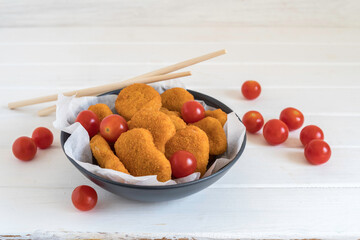 Chicken nuggets and cherry tomatoes in dark plate for simple snack.