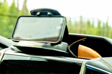 Mobile phone in a weighted clamshell clamp and sunglasses case on dashboard of vehicle with blurred trees in windshield - Soft focus